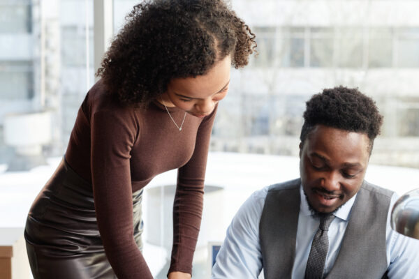 Vertical portrait of professional black man as boss with assistant signing documents at desk in private office